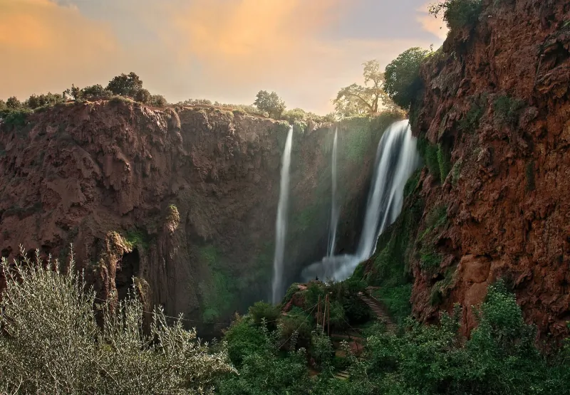 Waterfall pouring over red cliffs in the Middle Atlas, with olive trees in the foreground at golden hour