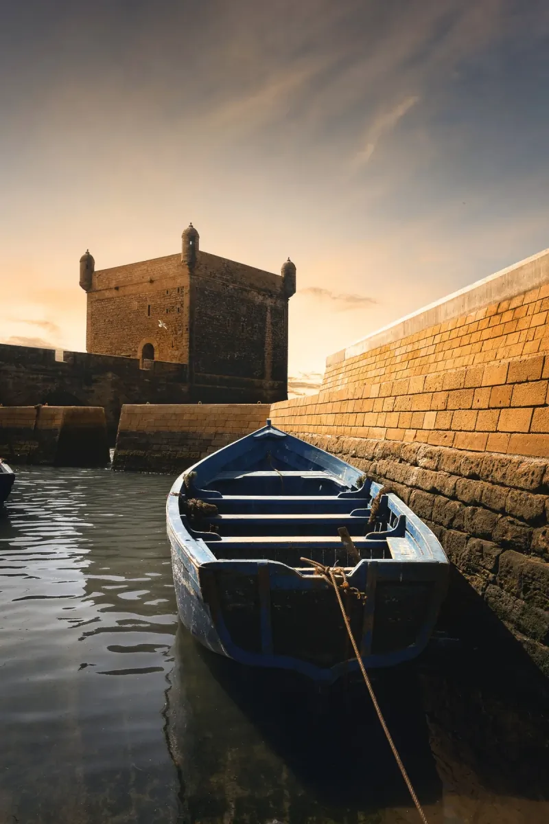 Wooden boat on the water below the stone ramparts of the Essaouira sqala at sunset