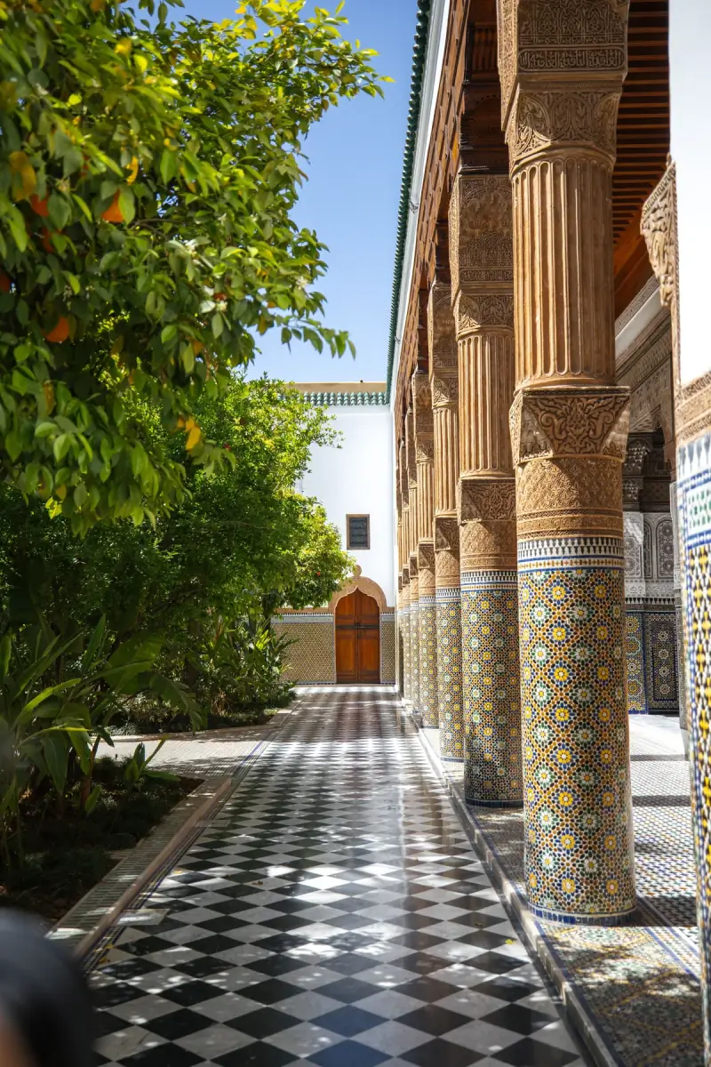 Sunlit riad courtyard in Marrakech with carved cedar columns, a chequered marble floor and orange trees
