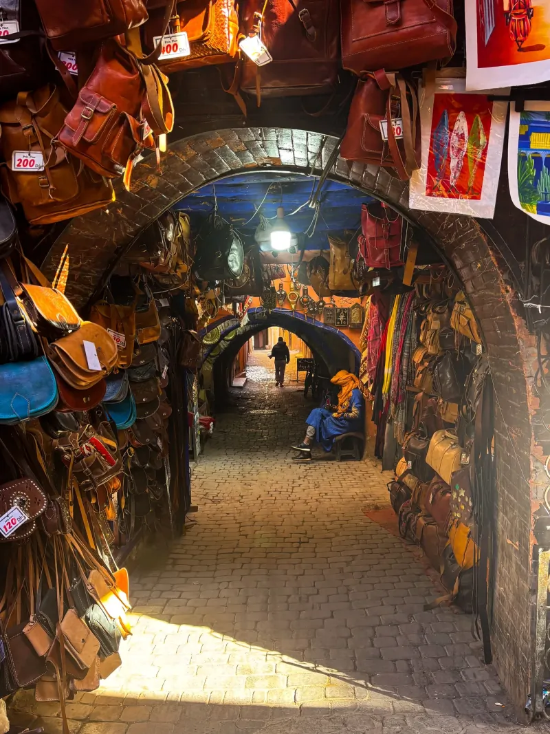 Covered souk alley in Marrakech hung with leather bags, slippers and painted crafts