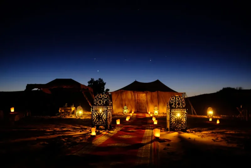 Lantern-lit desert camp tents at night under a starry sky in the Merzouga dunes