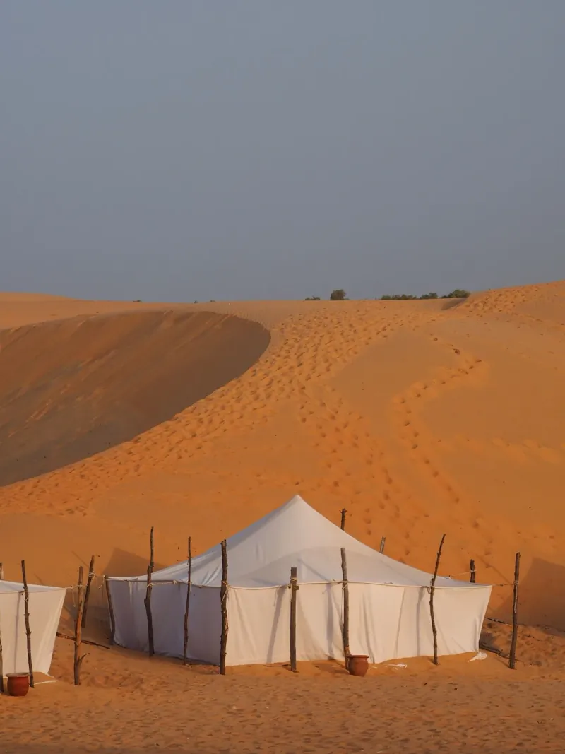 White canvas tents of a private camp at the foot of a tall sand dune near Merzouga