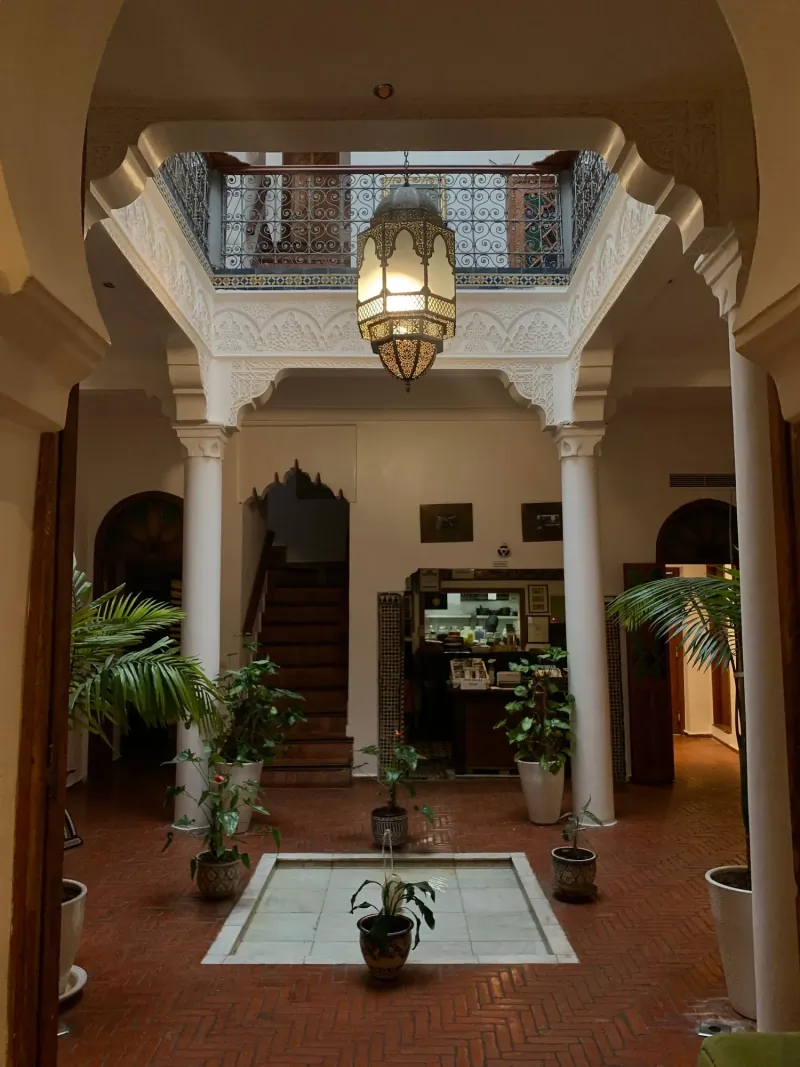 Two-storey riad courtyard with a hanging brass lantern, carved arches and a small fountain