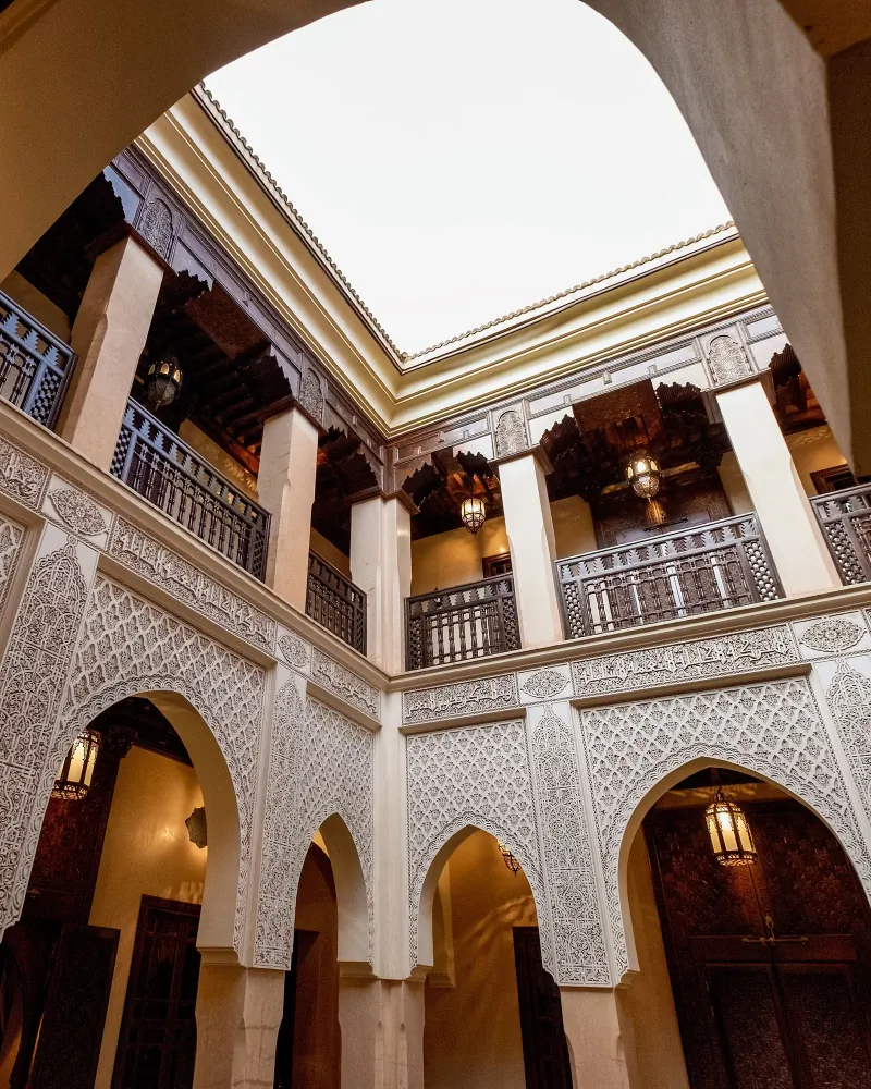 Riad courtyard seen from below, with ornate carved plaster arches and a skylight over the gallery