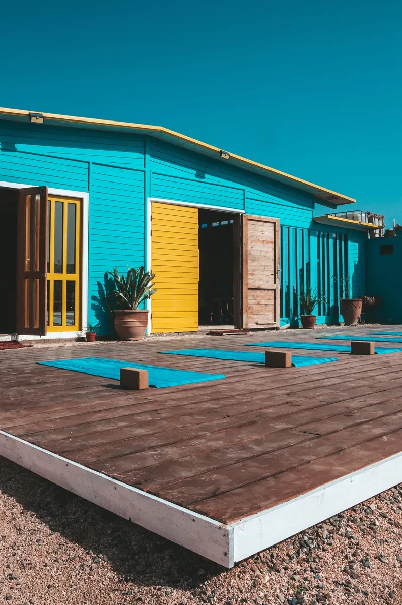 Turquoise-painted beach house with a wooden deck and yellow door in Taghazout