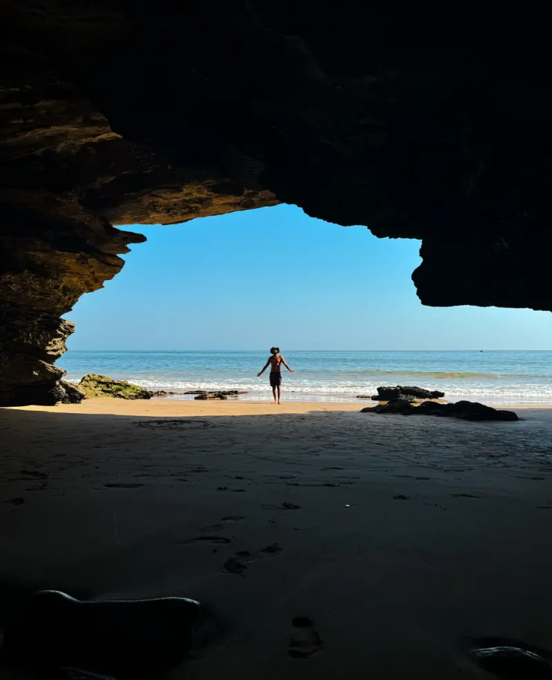 Silhouette of a person walking out of a sea cave onto the beach near Taghazout