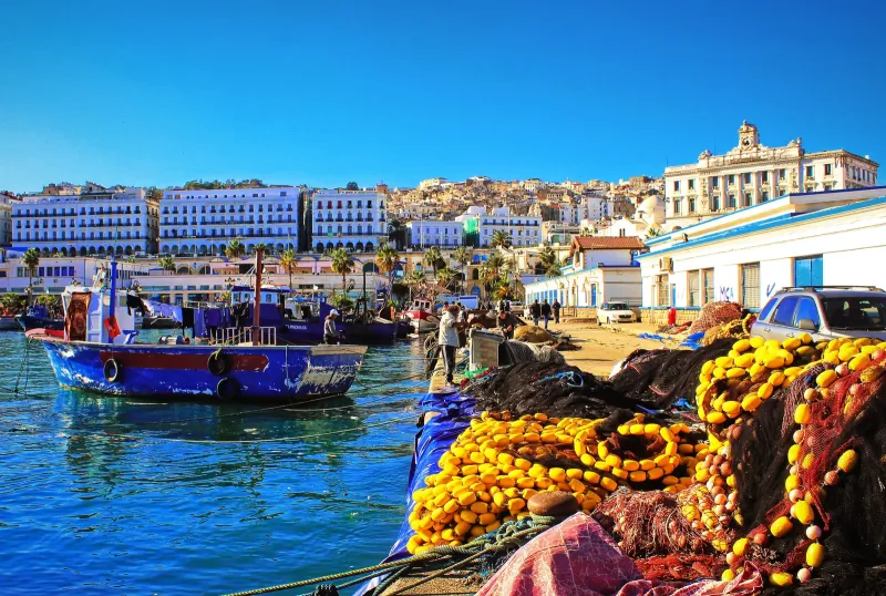 Blue fishing boats and piles of nets in Tangier's old port, with the white medina rising behind